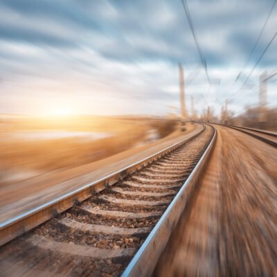 Railroad in motion at sunset. Railway station with motion blur effect and colorful sky with clouds. Industrial concept background. Railroad travel, railway tourism. Blurred railway. Transportation