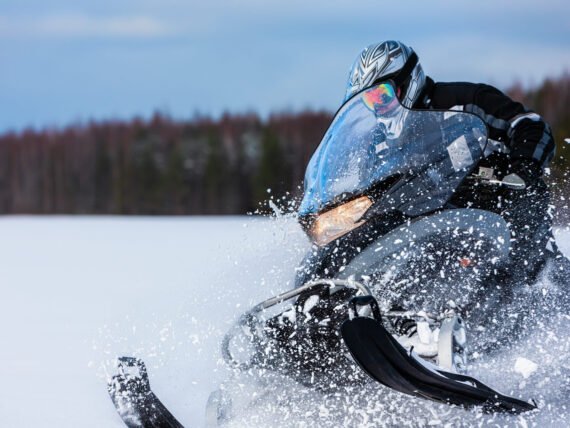 In deep snowdrift snowmobile rider driving fast. Riding with fun in white snow powder during backcountry tour. Extreme sport adventure, outdoor activity during winter holiday on ski mountain resort.