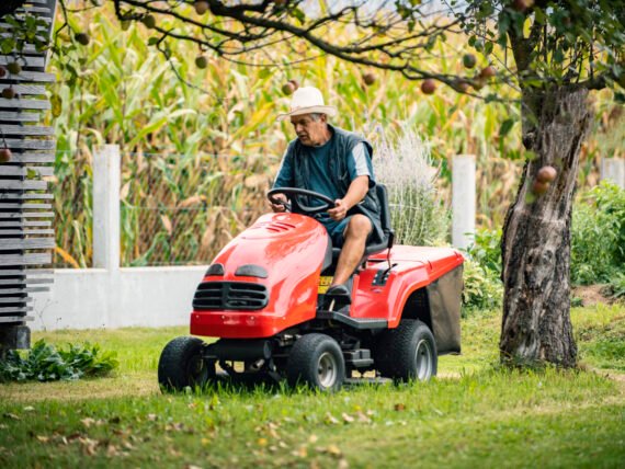 Worker man riding lawn mower mini tractor on a meadow grass