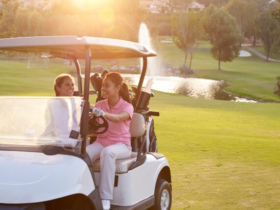 Female Golfers Driving Buggy Along Fairway Of Golf Course